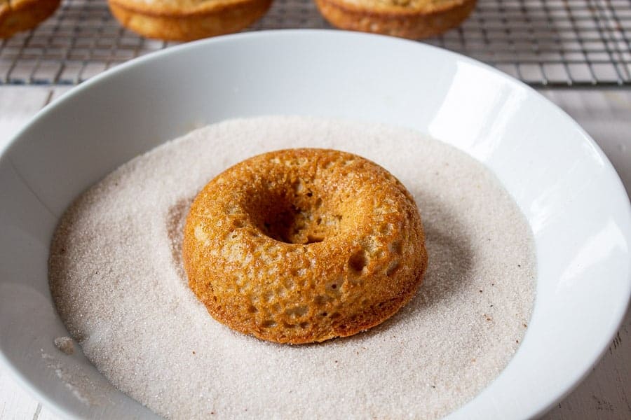 A baked donut in a bowl of spiced sugar.