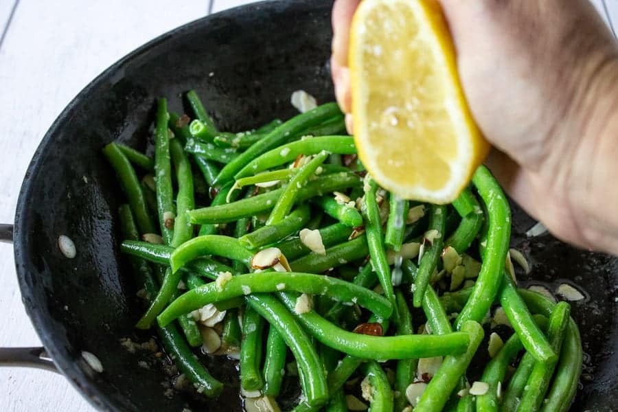 A lemon being squeezed over green beans in a pan. 