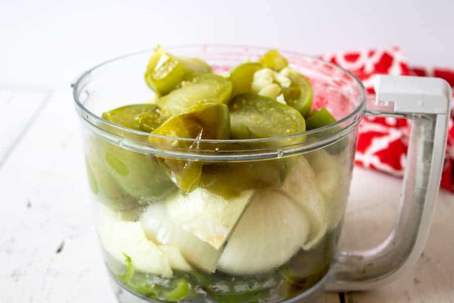 A food processor bowl filled with onions, peppers and tomatillos.