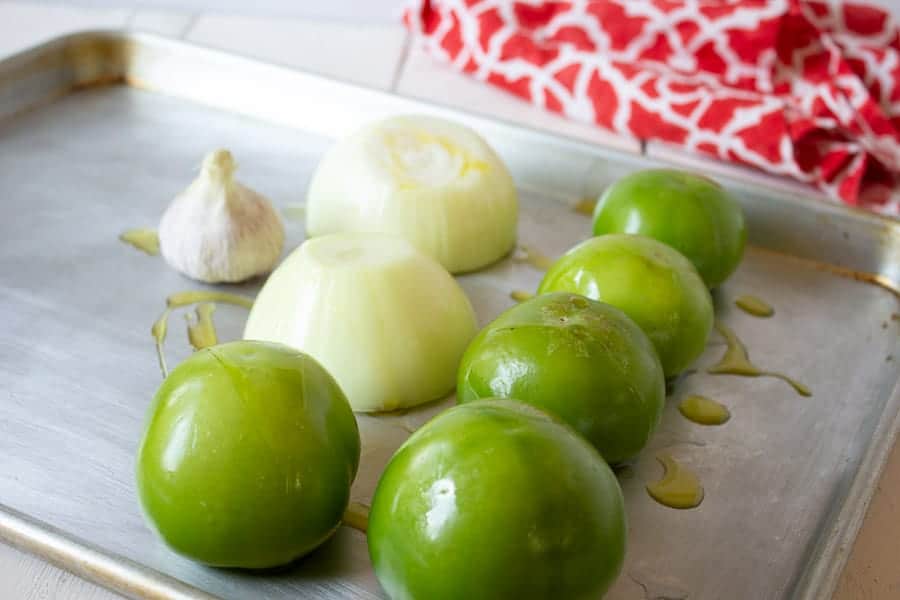 A baking tray with tomatillos, onions and garlic.