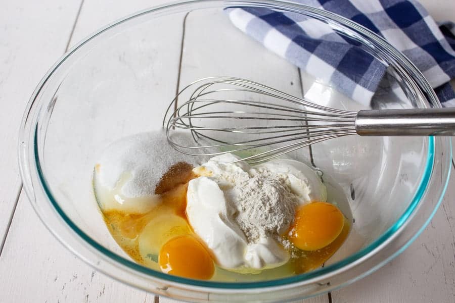 Eggs, sour cream, sugar and vanilla in a glass bowl.