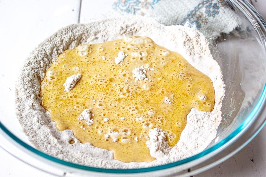 A glass bowl with flour and a wet mixture added on top.