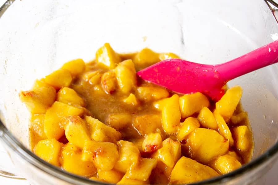 Chopped peaches in a bowl with a pink spatula.