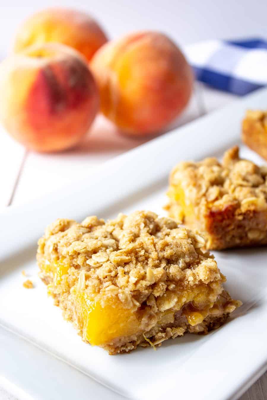Peach Crumb Bars on a white late with fresh peaches in the background.