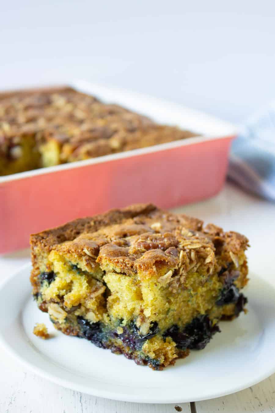 A slice of yellow cake with blueberries and pecans on a small plate. 