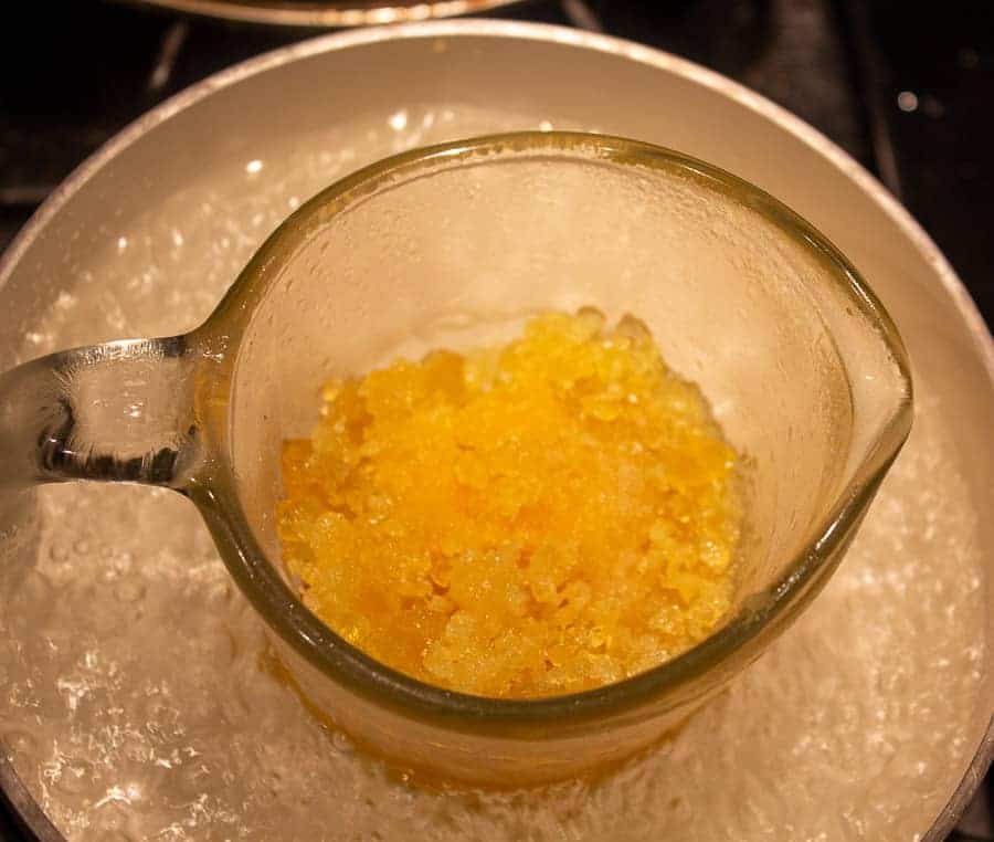 A glass measuring cup filled with beeswax and pine resin in a pot filled with boiling water.