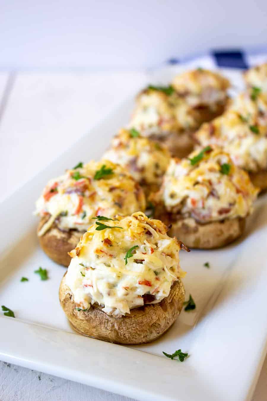 Mushrooms filled with crab and bacon lined up on a white platter.