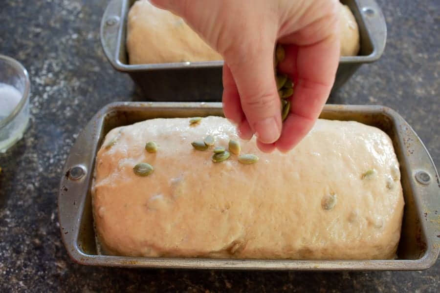 Pumpkin seeds being sprinkled on bread dough.