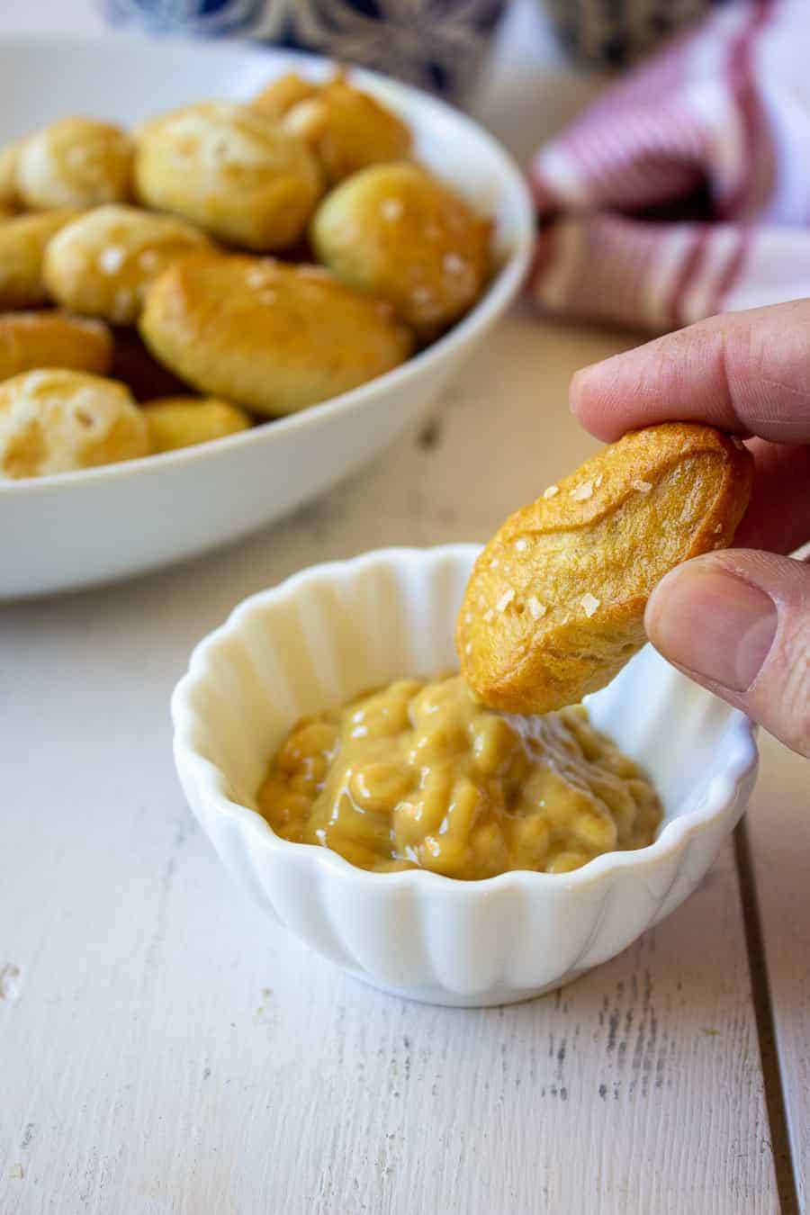 A small pretzel dipped into a bowl of mustard.