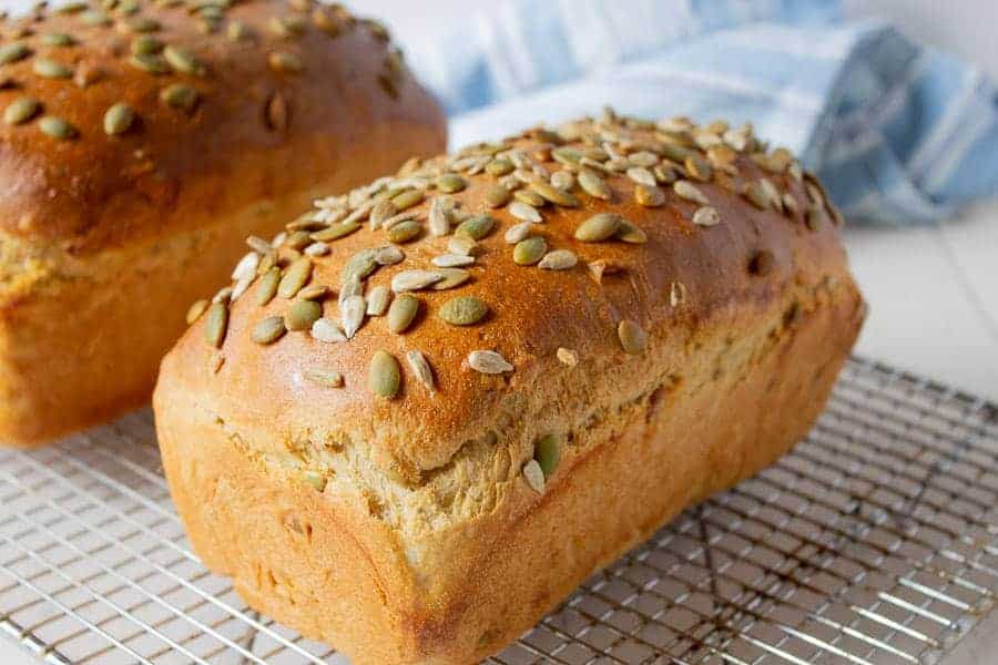 A loaf of bread topped with seeds sitting on a baking rack.