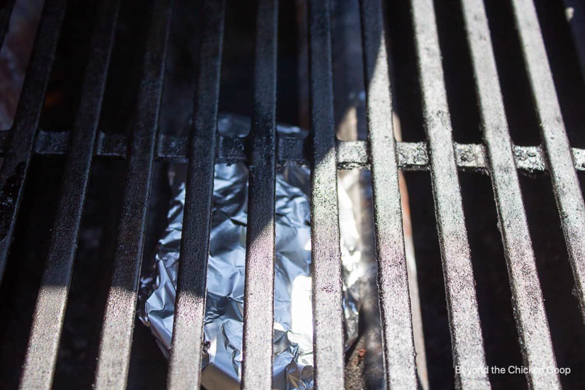 A gas grill with a foil packet below the grate.