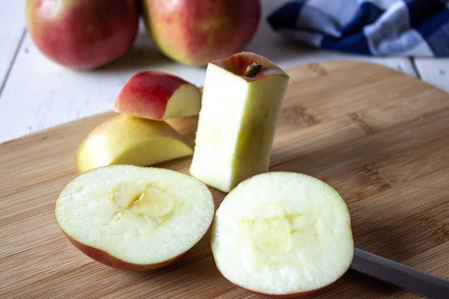 Apples being cored and sitting on a cutting board.