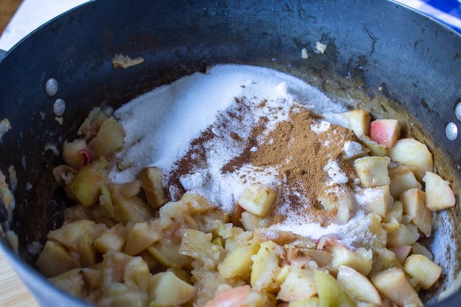 Cooked apples topped with sugar and cinnamon in a black pot.