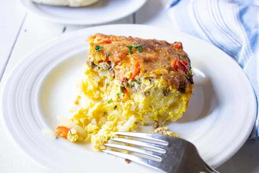 A breakfast casserole filled with eggs, hash browns and sausage on a white plate with a fork.