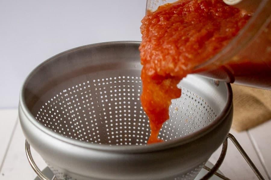 Tomato sauce being poured into a food mill. 