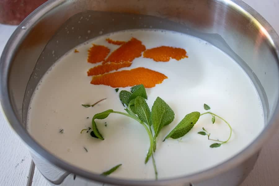 A sauce pot filled with cream, orange peel, and fresh herbs.