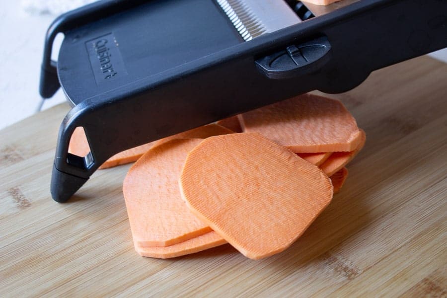 Sweet potatoes being cut on a mandoline.