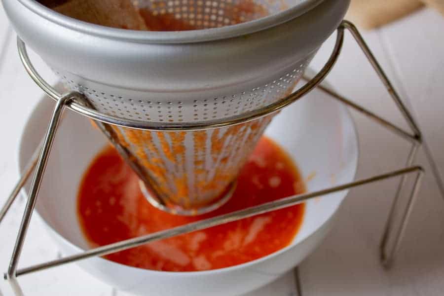 Smooth tomato sauce being extracted through a food mill. 