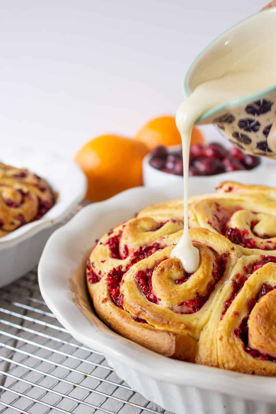 A glaze being poured over a pan of cranberry filled cinnamon rolls. 