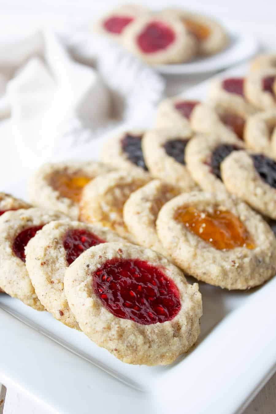 A white platter filled with cookies with different types of jam baked into the cookies. 