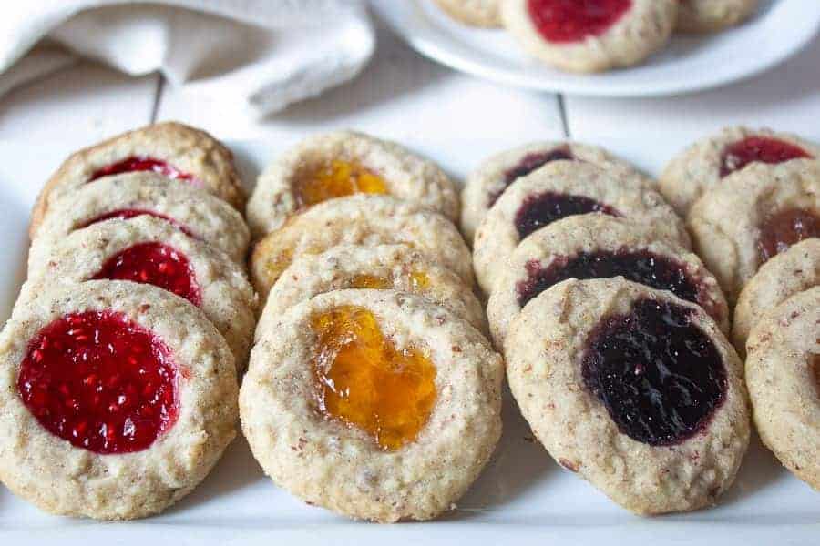 Thumbprint cookies with different types of jam on a white plate.