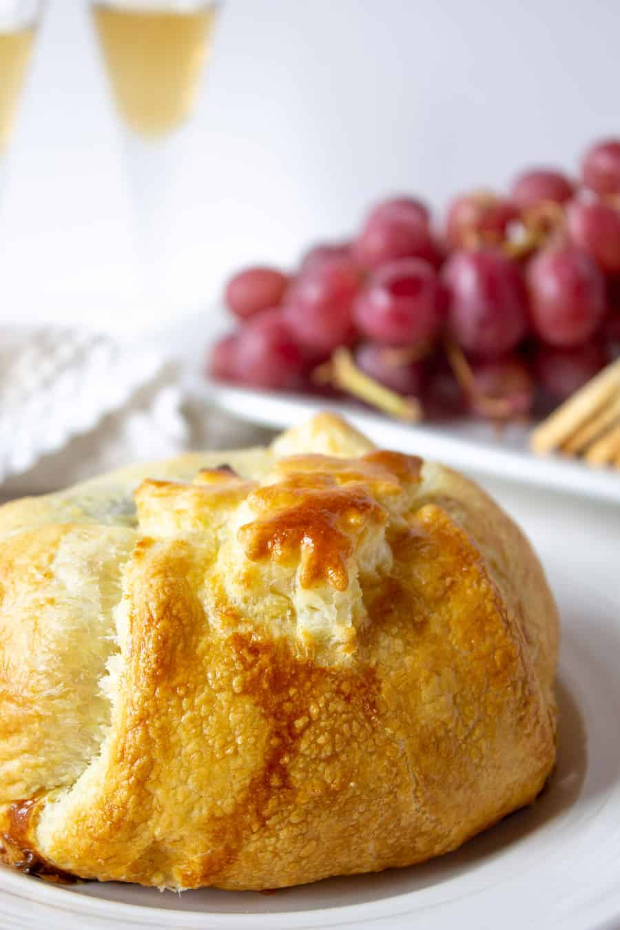 Golden puff pastry crust on a plate with red grapes in the background.