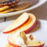 A cracker topped with an apple slice and a soft white cheese.