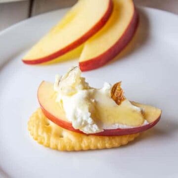 A cracker topped with an apple slice and goat cheese.
