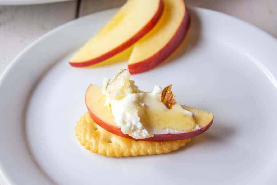 A cracker topped with an apple slice and goat cheese.