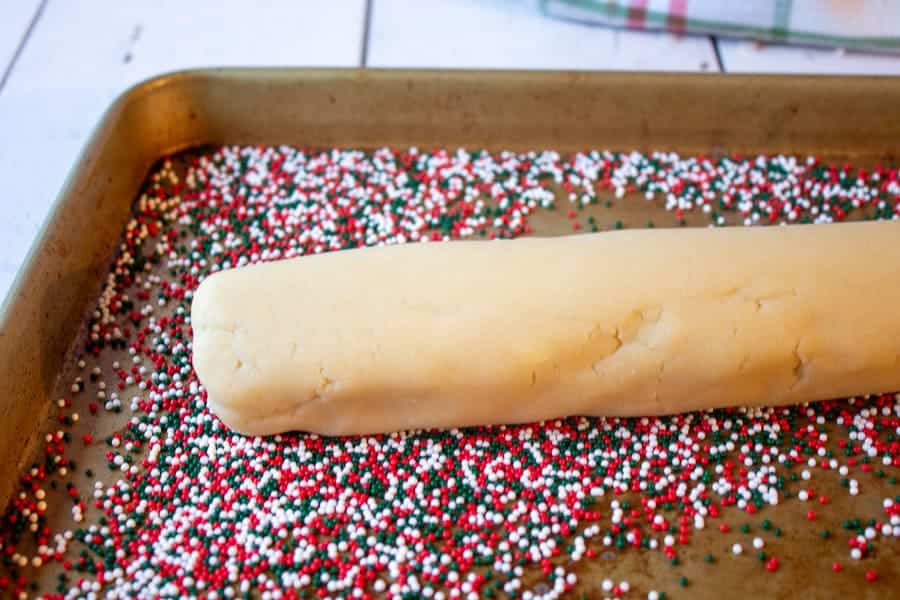 A cookie sheet covered with sprinkles with a log of cookie dough in the middle of the sprinkles.