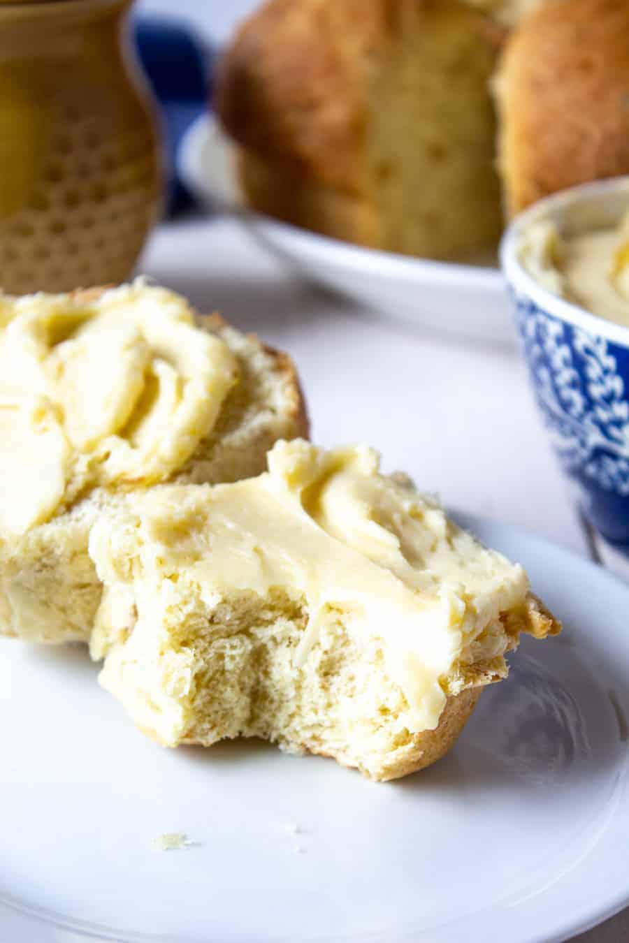 Homemade rolls topped with a light yellow spread on a white plate. 