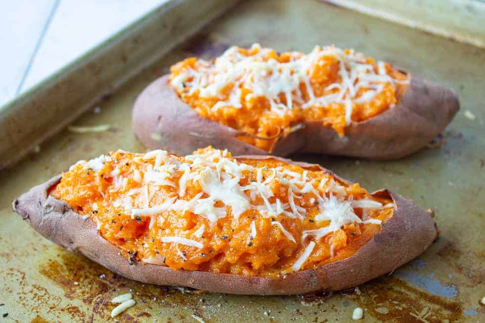 Twice baked sweet potatoes topped with shredded parmesan cheese on a baking sheet.