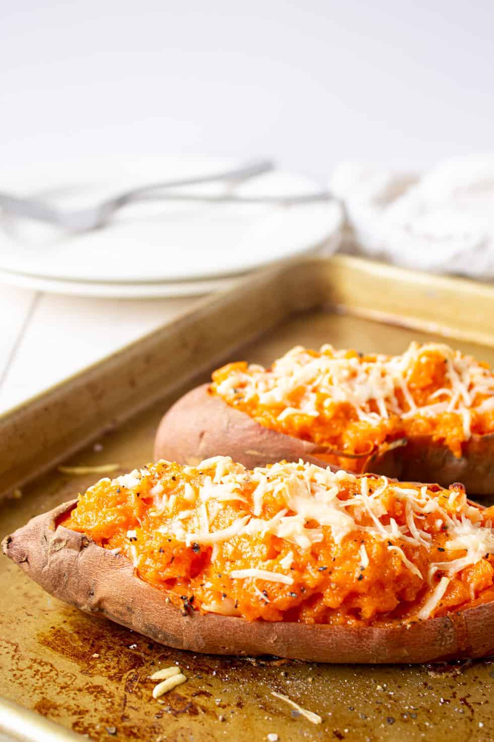 Sweet potatoes topped with cheese on a baking sheet.