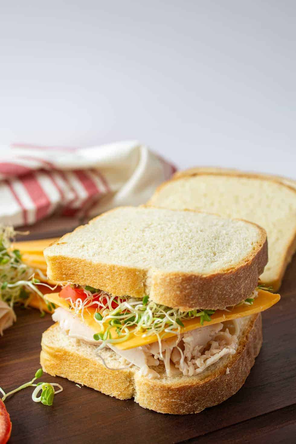 Turkey sandwich with tomatoes, cheese and sprouts on a brown board.