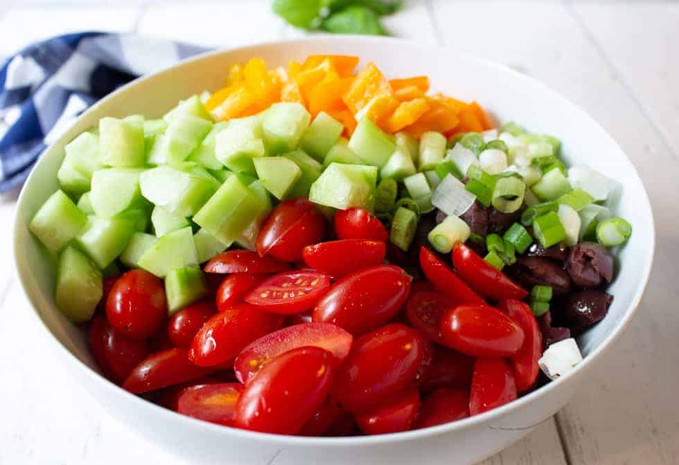 A large bowl filled with fresh chopped tomatoes, cucumbers and peppers. 