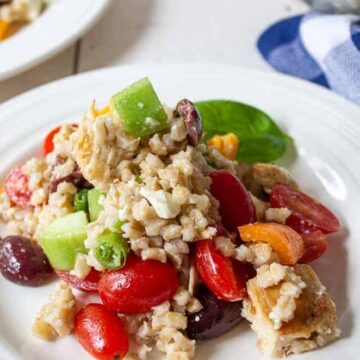 Salad with barley, tomatoes, olives and chicken on a white. plate.