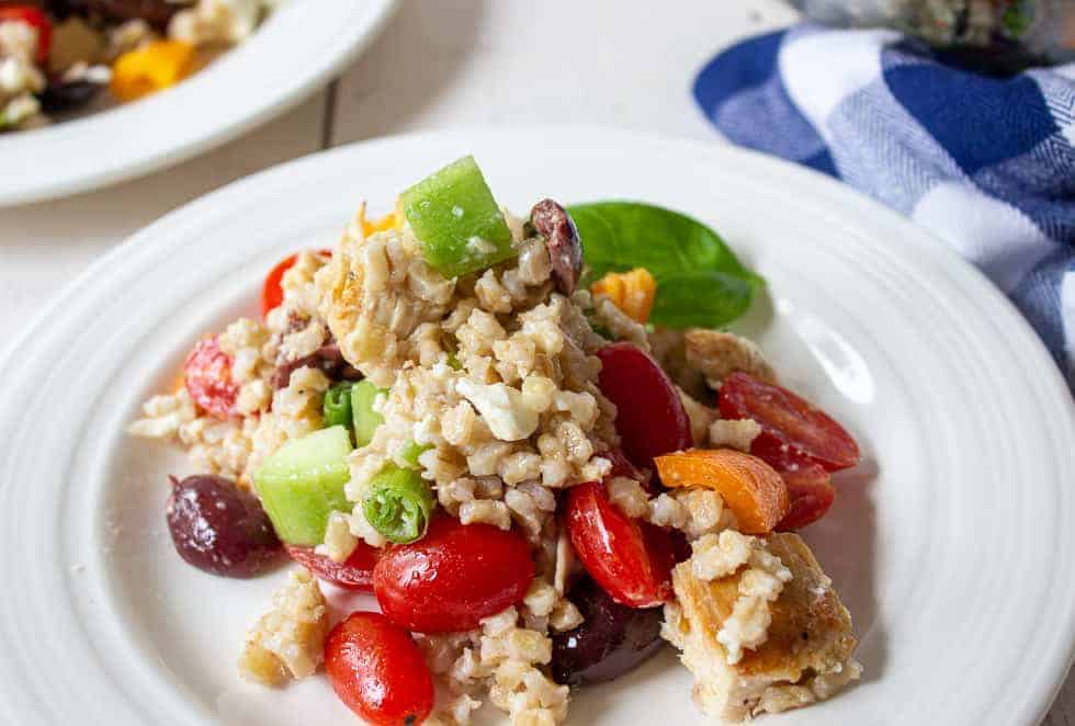 Salad with barley, tomatoes, olives and chicken on a white plate.