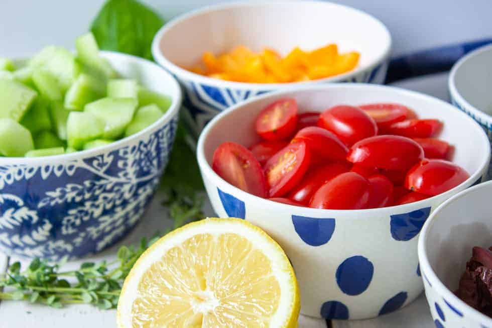 Small blue and white bowls filled with fresh tomatoes, cucumbers, peppers and olives. 