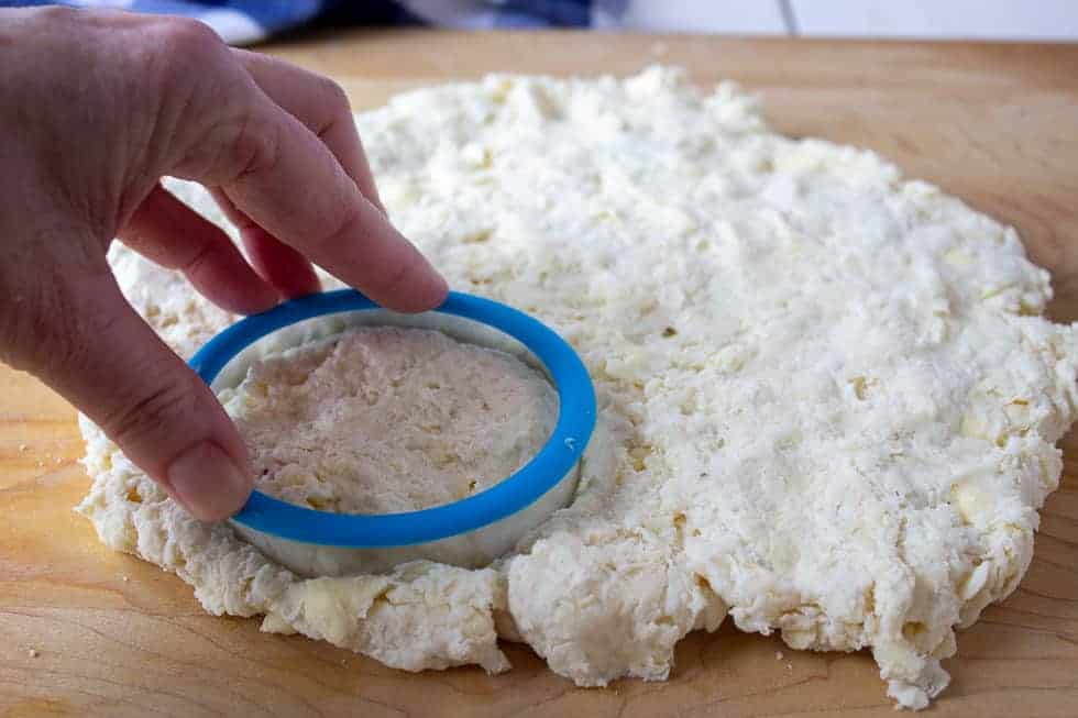 A round cutter being pressed into biscuit dough.