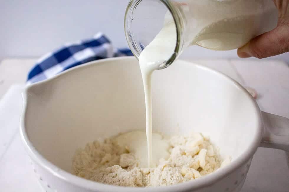 Buttermilk being poured into a bowl filled with a flour mixture.