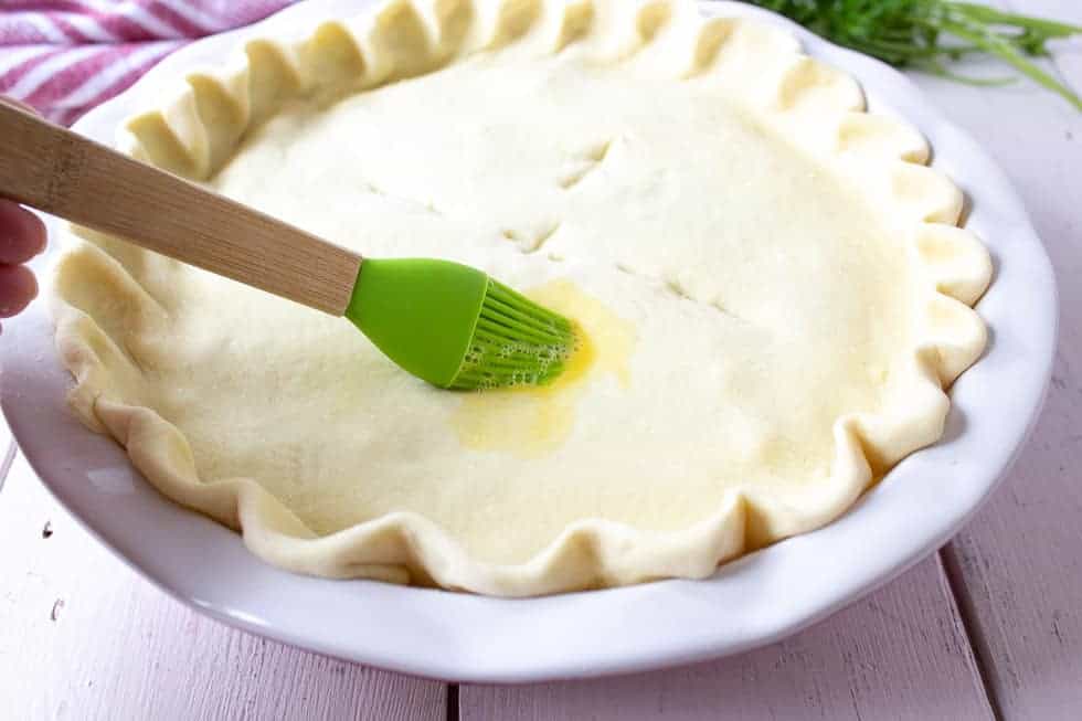 A green pastry brush adding an egg wash to a pie crust.