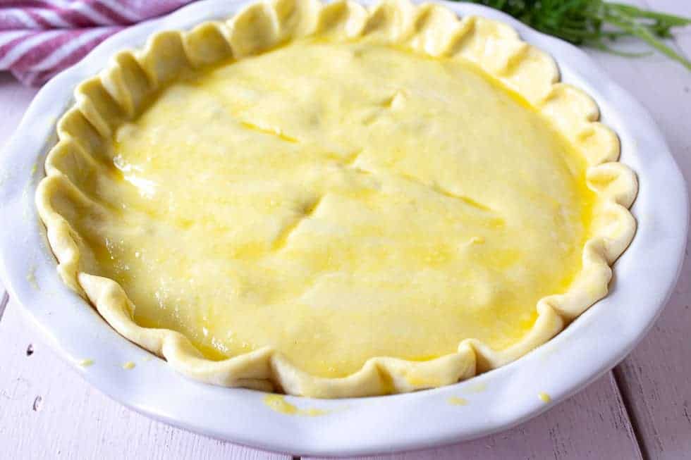 An uncooked chicken pot pie in a large white pie plate.