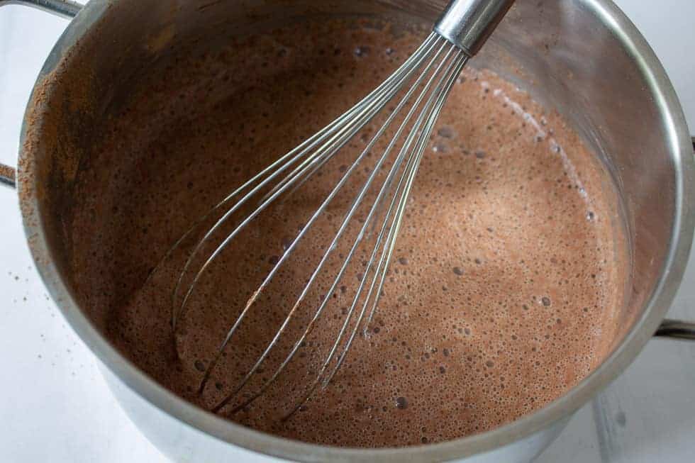 A whisk whipping up a chocolate mixture in a pan.
