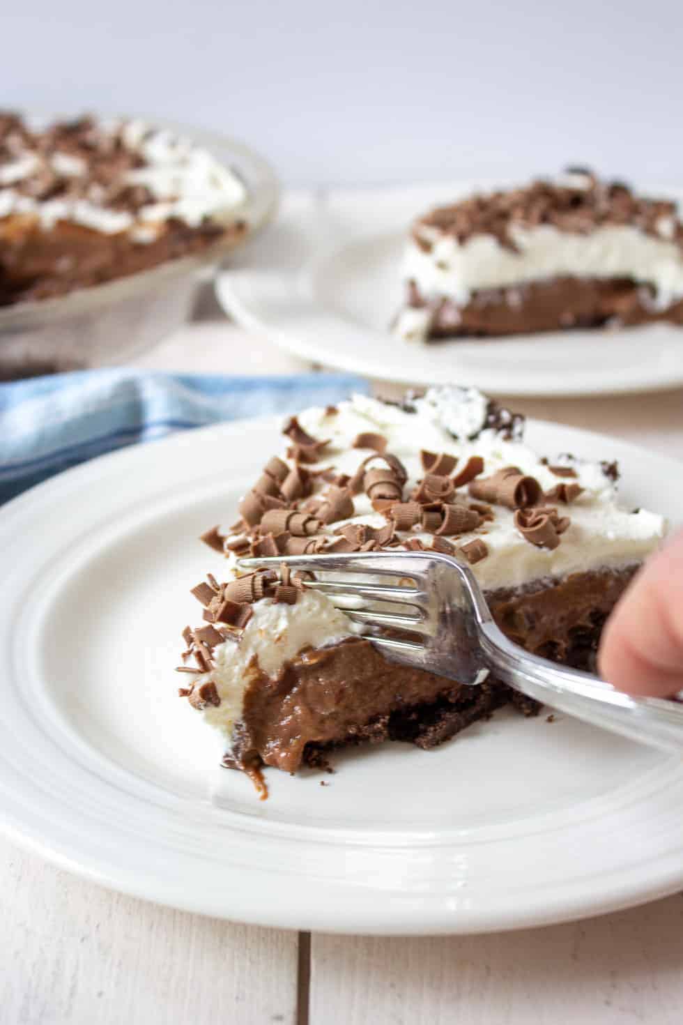 A fork slicing into a piece of chocolate pie topped with whipped cream. 