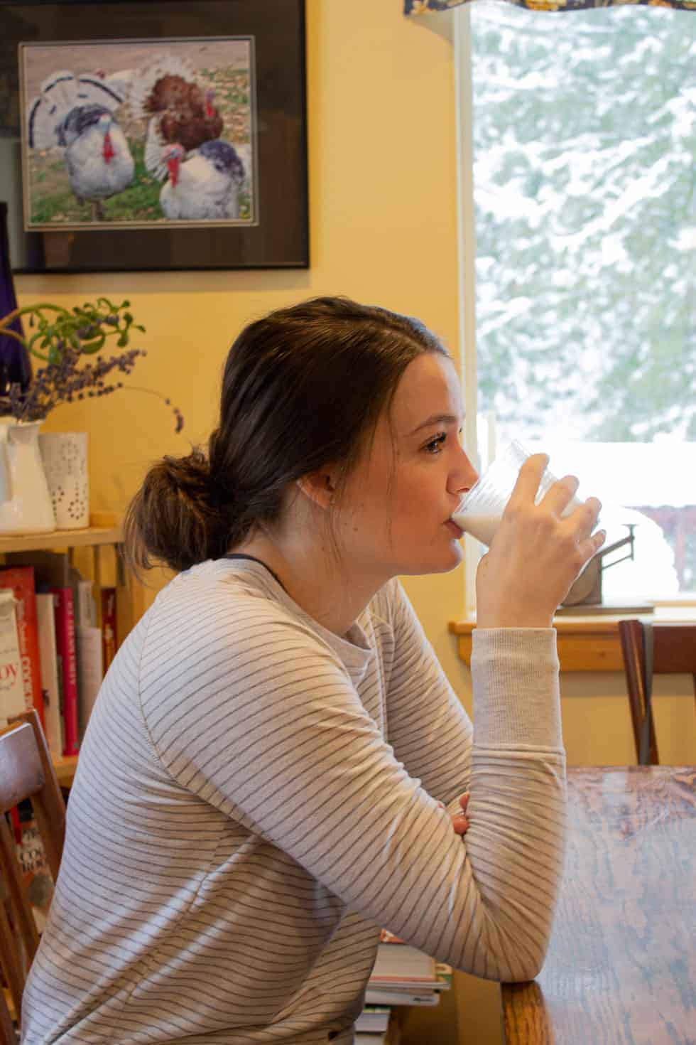 A girl drinking a glass of milk at a kitchen table. 