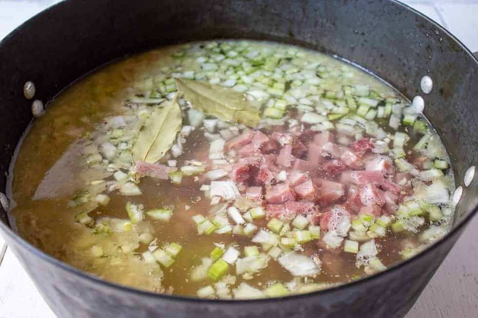 A pot of soup filled with ham, beans and fresh onions. 