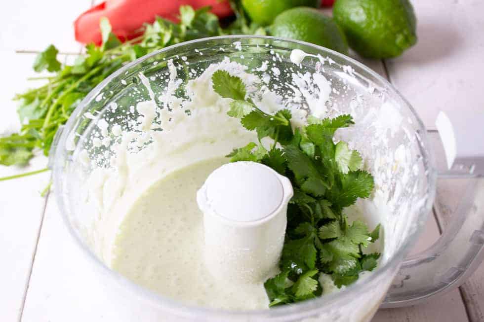 Fresh cilantro added to a creamy mixture in a food processor.