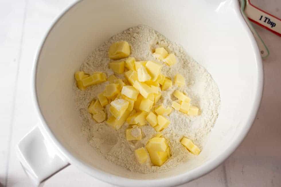 Small cubes of butter in a white bowl filled with flour.