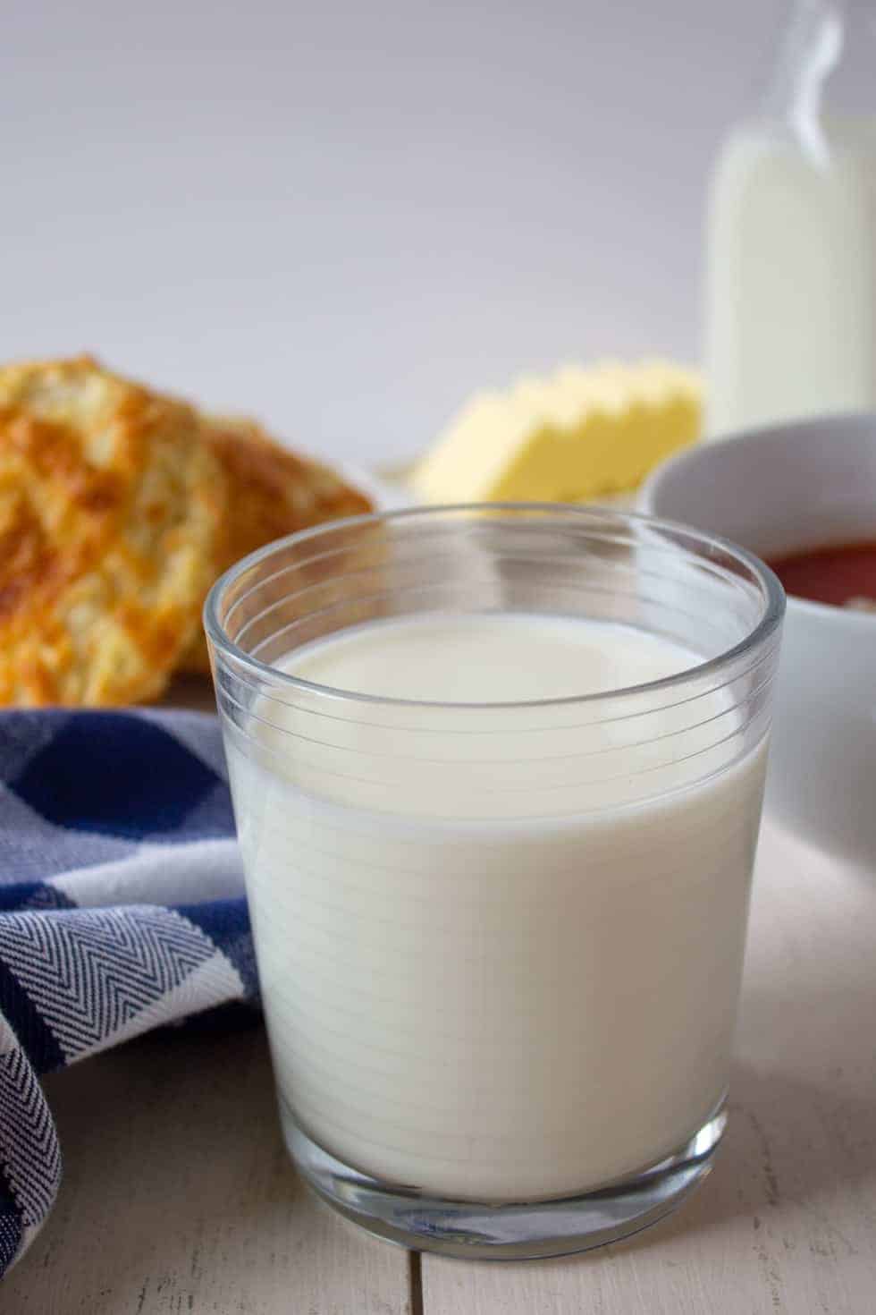 A glass of milk on a table with soup and biscuits. 