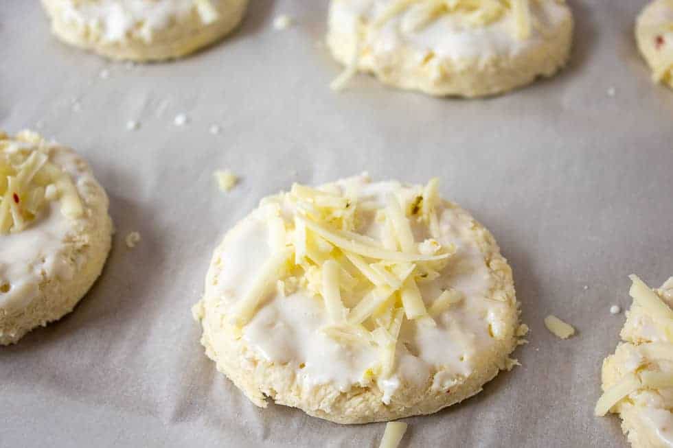 An uncooked biscuit topped with shredded cheese.